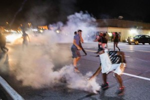A protester picks up a gas canister to throw back towards the police after tear gas was fired at demonstrators reacting to the shooting of Michael Brown in Ferguson, Missouri