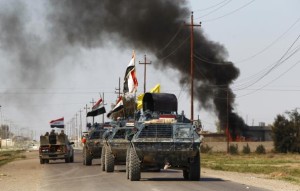 Armored vehicles of Iraqi security forces with militias known as Hashid Shaabi are driven past smoke arising from a clash with Islamic State militants in the town of al-Alam